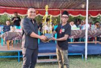 Ketua PSSI Manggarai Barat, Marianus Yono Jehanu atau yang akrab disapa Yono Jehanu, menyerahkan bantuan piala kepada Ketua Panitia Abdul Gani pada Turnamen Bola Voli Putra dan Putri Idul Adha Cup 1447 H yang berlangsung di Lapangan Soknar, Desa Golo Mori, Kecamatan Komodo, Kabupaten Manggarai Barat, Minggu (7/6/2026) sore. Foto Rino/GBRNews.id