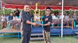 Ketua PSSI Manggarai Barat, Marianus Yono Jehanu atau yang akrab disapa Yono Jehanu, menyerahkan bantuan piala kepada Ketua Panitia Abdul Gani pada Turnamen Bola Voli Putra dan Putri Idul Adha Cup 1447 H yang berlangsung di Lapangan Soknar, Desa Golo Mori, Kecamatan Komodo, Kabupaten Manggarai Barat, Minggu (7/6/2026) sore. Foto Rino/GBRNews.id

